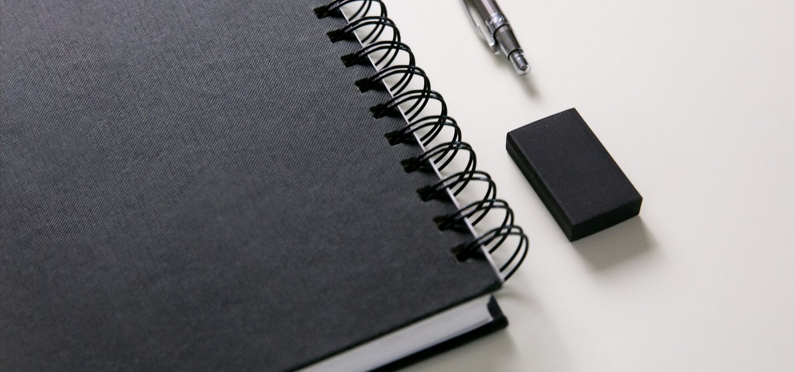 Demande de devis gratuit et contact Carnet à spirale noir et stylo posés sur un bureau clair